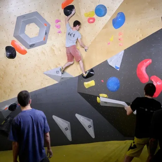 Соревнования по скалолазанию в закрытом спортзале с участниками на фоне цветных зацепов в вечернее время