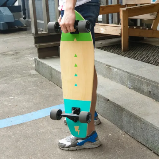 Молодой человек держит скейтборд, стоя на улице у здания в солнечный день