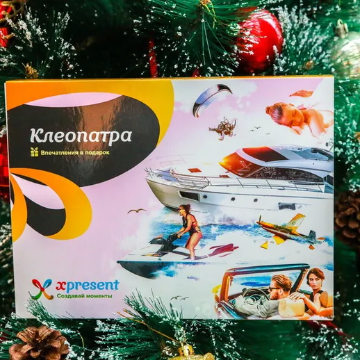 Подарочная упаковка игры «Клеопатра» на фоне новогодней ели с украшениями