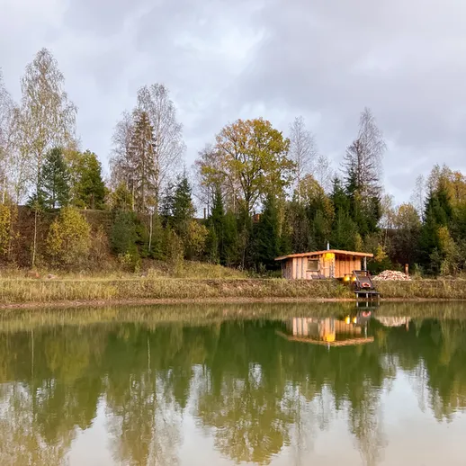 Природа у озера осенью с отражением домика и леса на берегу в спокойной обстановке