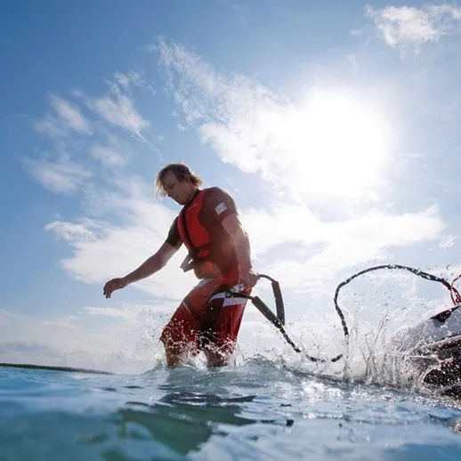 Мужчина на воде с гидрошлемом выполняет трюк на водном скейтборде в солнечный день на озере