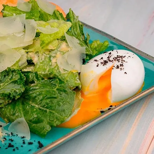 Яйцо-пашот на салате с листовой зеленью и тертым пармезаном, поданное на голубой тарелке