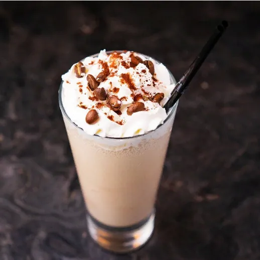 Вкусный кофе с взбитыми сливками и орехами, поданный в прозрачном стакане на темном фоне