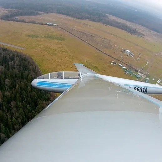 Полет планера над лесами и полями в облачную погоду в районе малонаселенной местности