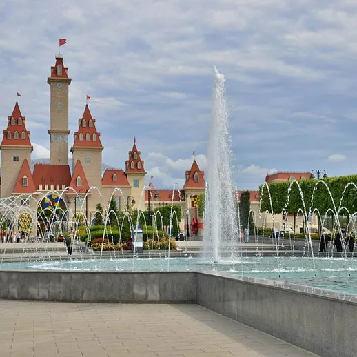 Прекрасный фонтан и замок на фоне яркого неба в парке развлекательных аттракционов