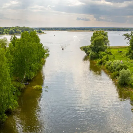 Спокойная река с зелеными берегами и лодкой летом на закате