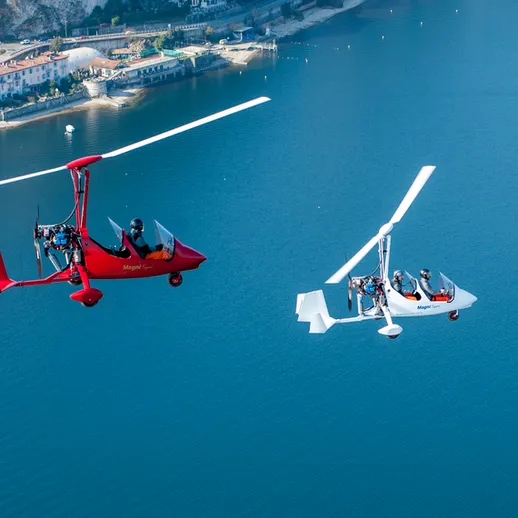 Два легких вертолета взлетают над красивым озером в ясный солнечный день