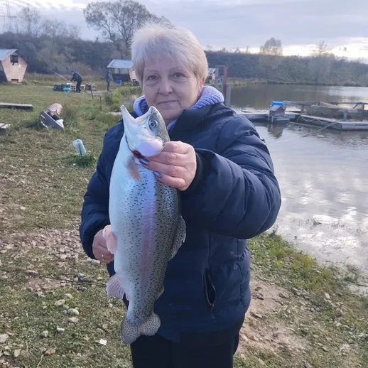 Женщина с крупной форелью на берегу водоема в осенний день