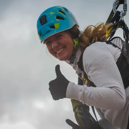 Молодая женщина в каске демонстрирует уверенность во время парапланеризма на фоне облачного неба