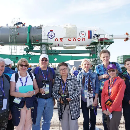 Группа людей с фотоаппаратами у ракеты во время экскурсии на космодроме в России в ясный солнечный день