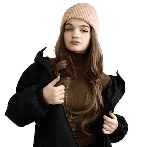 Молодая женщина в теплой куртке и шапке на фоне белой стены