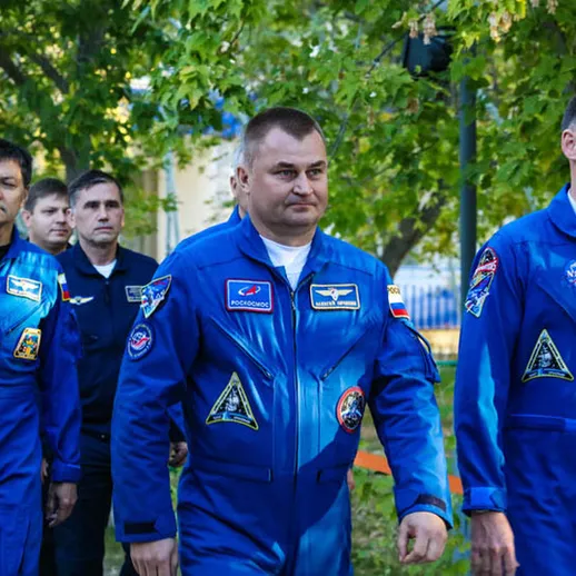 Космонавты в синих комбинизонах идут к ракете на старте в Казахастане в солнечный день