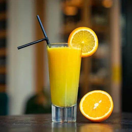 Вкусный освежающий апельсиновый сок в стакане с трубочкой на столе в кафе