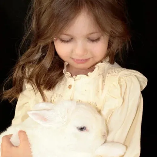 Маленькая девочка в белой рубашке держит пушистого белого кролика на руках, улыбается и наслаждается моментом счастья