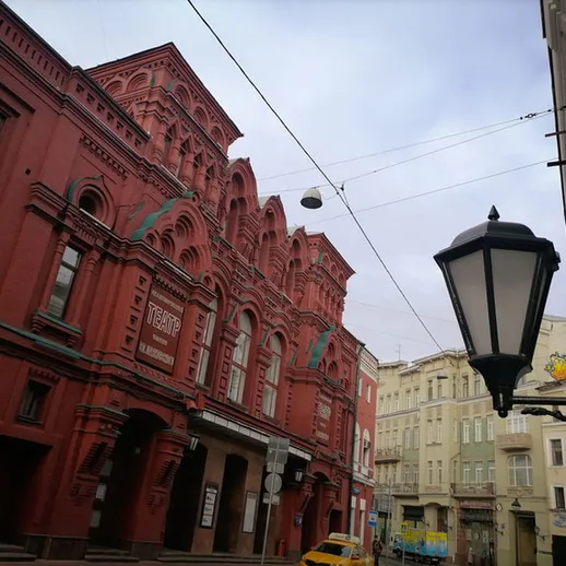 Здание театра на улице в Москве, яркая красная архитектура среди серых домов и пасмурное небо