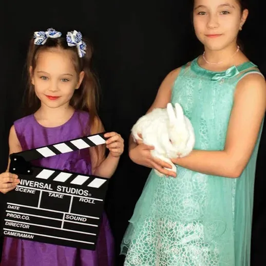 Две девочки в костюмах с киноаппаратурой и зайцем на черном фоне