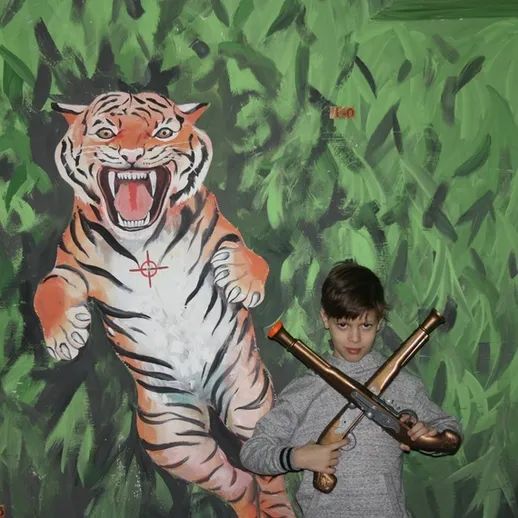 Мальчик позирует с игрушечными пушками у стен росписи тигра в развлекательном центре