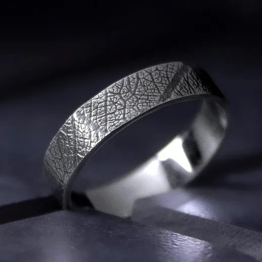 Металлическое обручальное кольцо с текстурой, расположенное на деревянной поверхности при естественном освещении