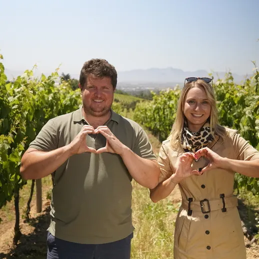 Пара на винограднике показывает сердечки и улыбается под солнечным небом