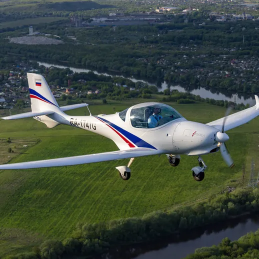 Маленький самолёт совершает полёт над живописным пейзажем реки и зелеными холмами в России в ясный день