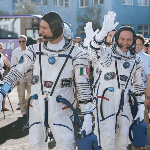 Космонавты в скафандрах во время подготовки к запуску на космический корабль на фоне зрителей и учреждений