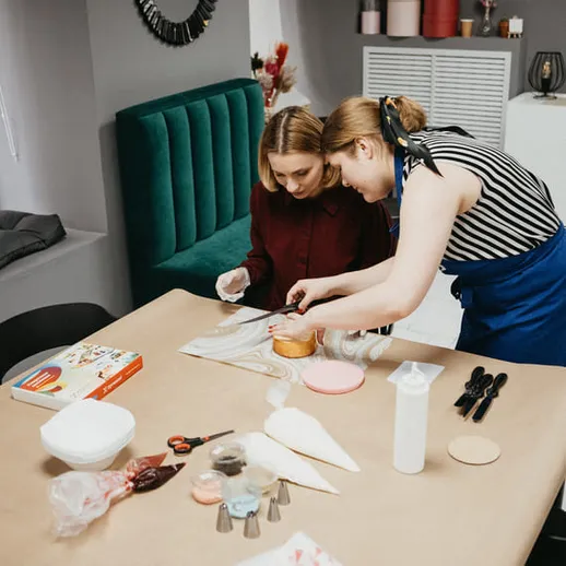 Две женщины готовят десерт на кухне, используя кондитерские инструменты и материалы для украшения тортов