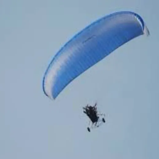 Парапланерист на голубом параплане в ясном небе над живописным пейзажем