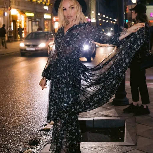 На улице ночью девушка в цветном платье и шляпе демонстрирует стильный наряд