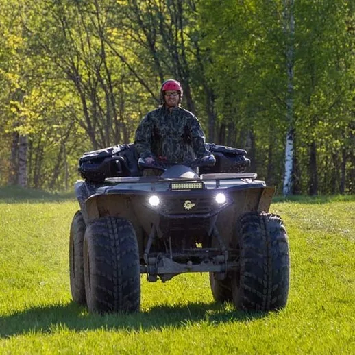 Мужчина на квадроцикле движется по зелёному лугу в солнечный день в лесной местности