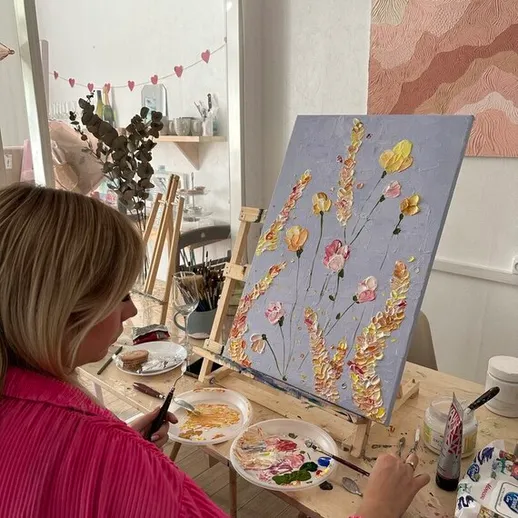 Женщина рисует цветочную картину в художественной студии с натуральным освещением в уютной обстановке
