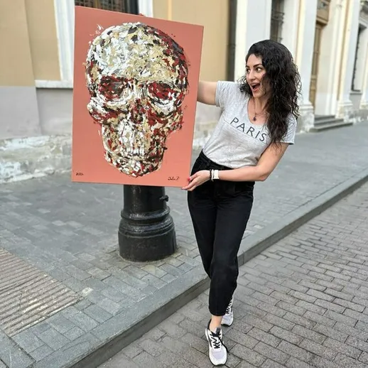 Молодая женщина держит картину черепа на улице города во время солнечного дня