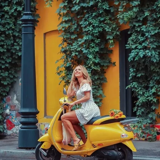 Молодая женщина на желтом скутере в городе, окруженном зелеными растениями и яркими стенами