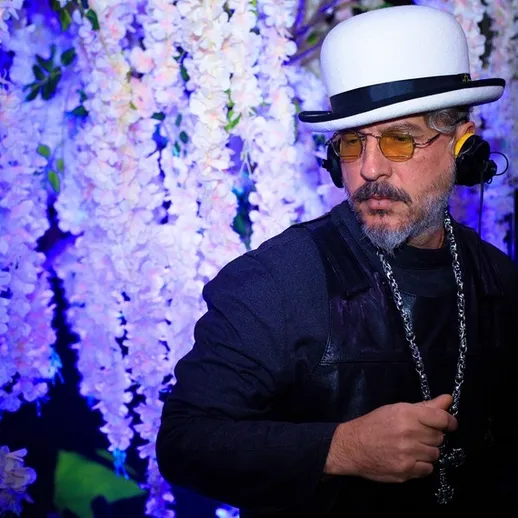 Музыкант с наушниками и цилиндром на фоне цветущих деревьев ночью на вечеринке