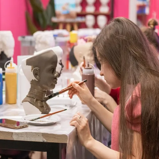 Девушка раскрашивает скульптуру в мастерской искусств в яркий день