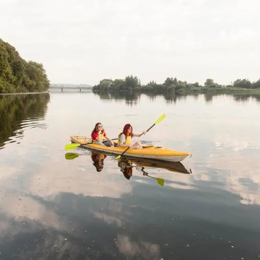 Две девушки катаются на каяке по спокойной реке под облачным небом