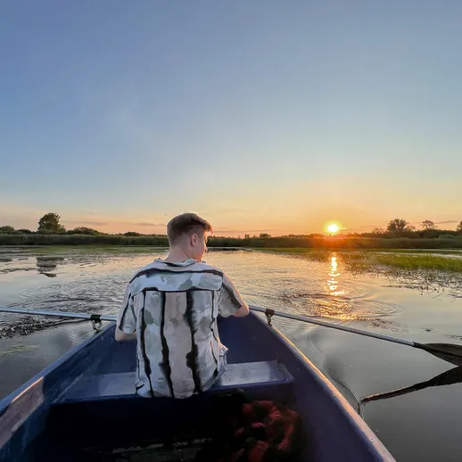 Молодой человек гребёт на лодке по реке на закате, наслаждаясь спокойствием природы