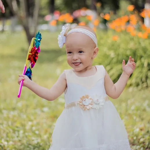 Ребёнок в белом платье с цветным цветком в парке среди зелени и цветов