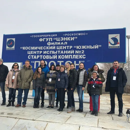 Группа людей у знака космического центра на старте испытаний в комплексном центре в феврале