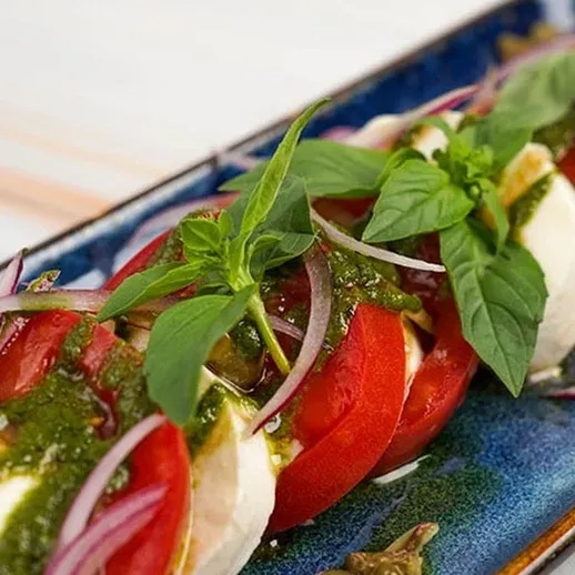 Капрезе с помидорами, моцареллой и базиликом на синей тарелке в уютном ресторане