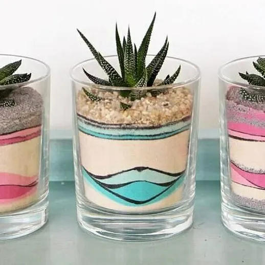 Уютные цветочные композиции в стеклянных горшках с кактусами, оформленные разноцветным песком и выставленные в ярком интерьере