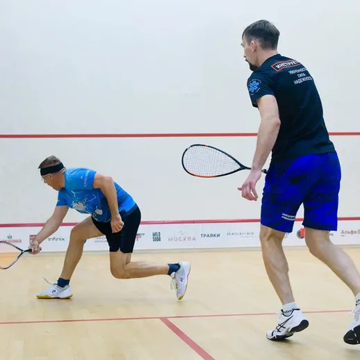 Два игрока в сквош соревнуются на корте в спортзале в вечернее время