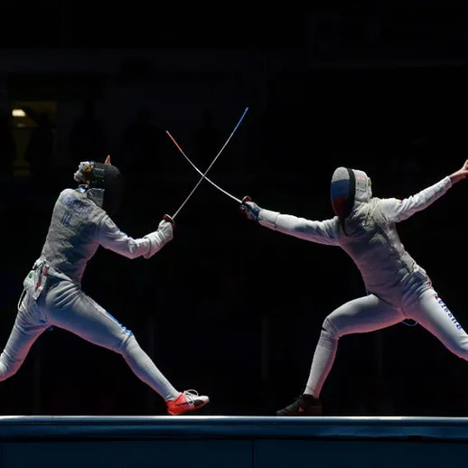 Фехтование на конкурсе, где два спортсмена сражаются на арене под яркими огнями в вечернее время