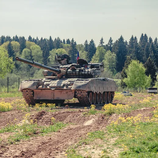 Танк Т-80 на зеленом поле с дикими цветами в солнечный день в лесистой местности