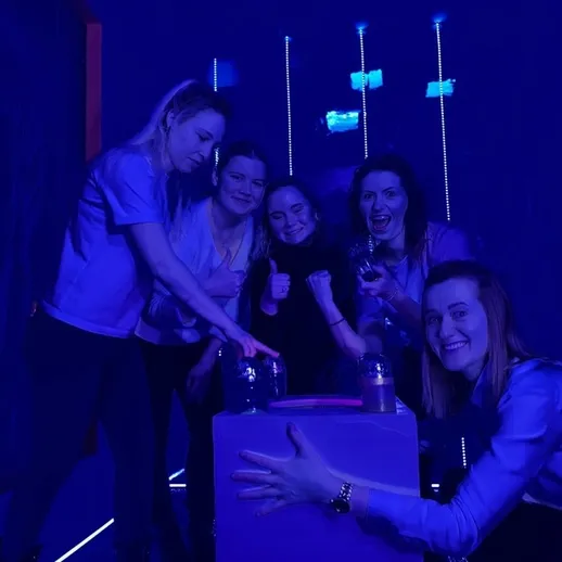 Группа из пяти женщин участвует в интерактивной игре в темной комнате с фиолетовым освещением