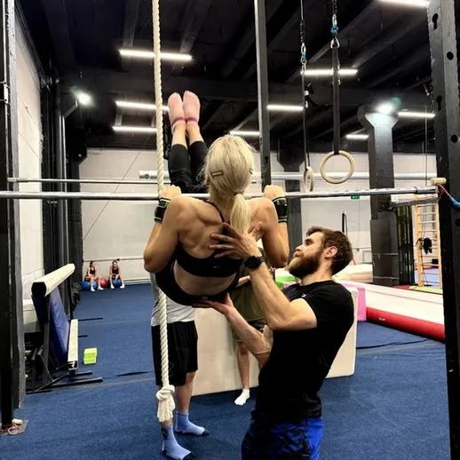 Тренировка по гимнастике в спортивном зале с использованием каната и поддержки тренера