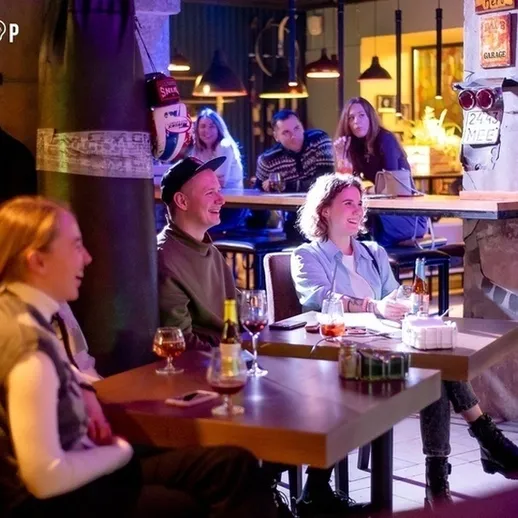 Веселая компания наслаждается вечерним мероприятием в уютном баре, обсуждая выступление комика в Москве