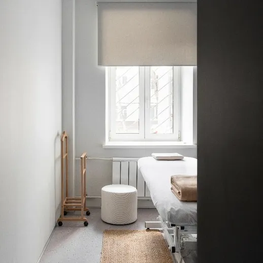 Уютный кабинет для процедур с массажным столом и окнами, освещающими пространство солнечным светом