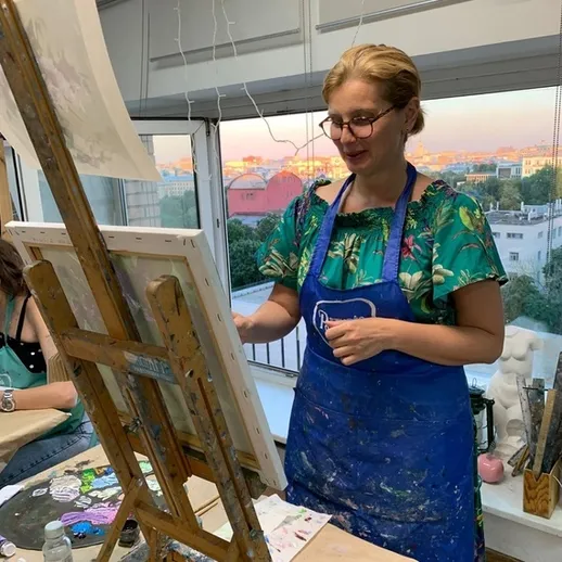 Художник в студии рисует картину на холсте при вечернем свете