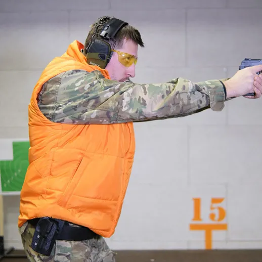 Тренировка стрельбы в тире с использованием пистолета выполняется мужчиной в оранжевом жилете