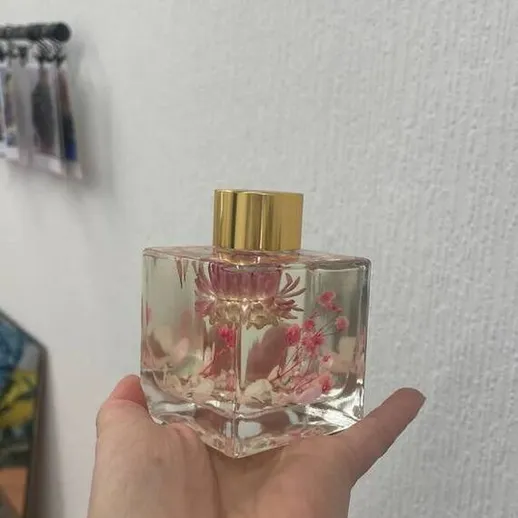 Флакон с парфюмом в руке на фоне стены и других предметов